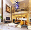 Massive blue, black, and white artisan blown glass chandelier suspended in a grand luxury living room with a mezzanine balcony.