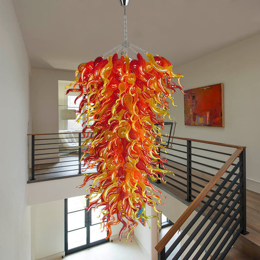 Dramatic red and yellow custom hand blown art glass chandelier installed in a contemporary home over a bright, two-story staircase and landing.