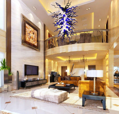 Massive blue, black, and white artisan blown glass chandelier suspended in a grand luxury living room with a mezzanine balcony.