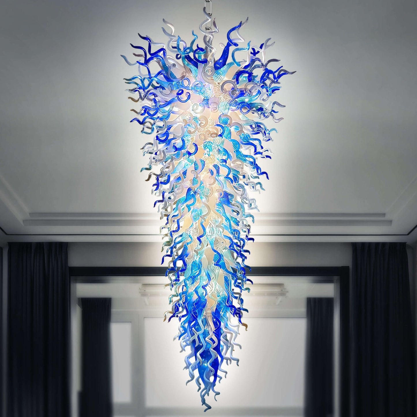 Giant blue and white hand-blown glass chandelier in a dramatic inverted cone shape, shown in a modern interior setting.
