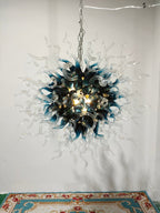 Artisan blue and clear glass starburst chandelier hanging against a minimalist white wall in a bright studio gallery