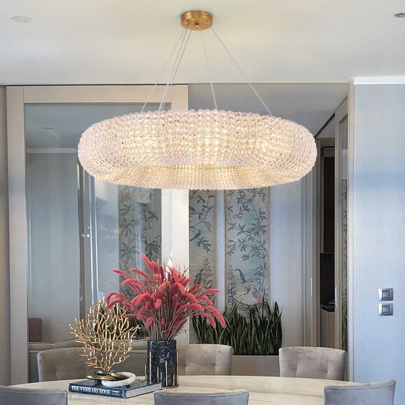 Large circular crystal pendant light installed in a luxury dining room above a modern table.