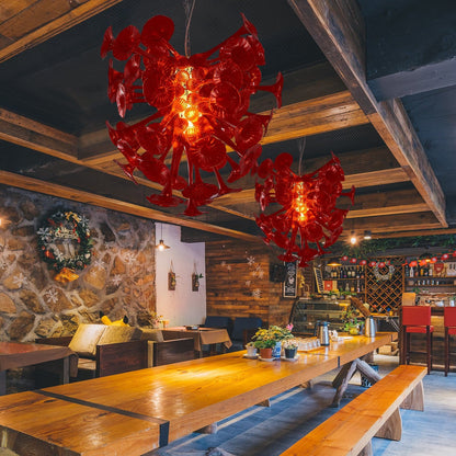 Dual Crimson Calla Lily chandeliers installed in a rustic-modern restaurant, casting a warm red glow over long wooden tables.