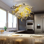 Chic kitchen interior with an artistic yellow blown glass chandelier hanging over a modern kitchen island with bar stools.