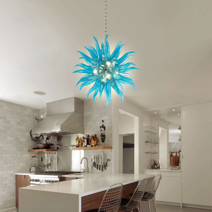 Modern ice-blue glass art chandelier centered over a contemporary kitchen island with white cabinetry and minimalist bar stools.