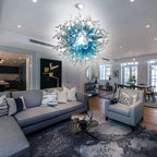 Spacious contemporary living room with gray furniture and a large blue blown glass art chandelier hanging in the center.