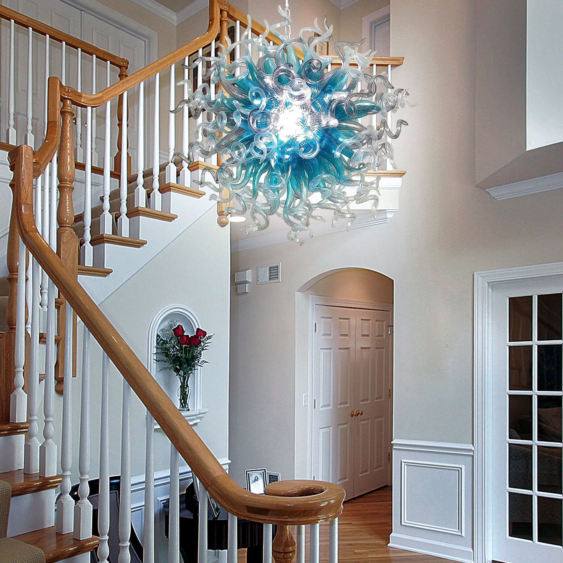 Artistic blue glass chandelier installed in a two-story foyer next to a wooden staircase for a grand entrance.