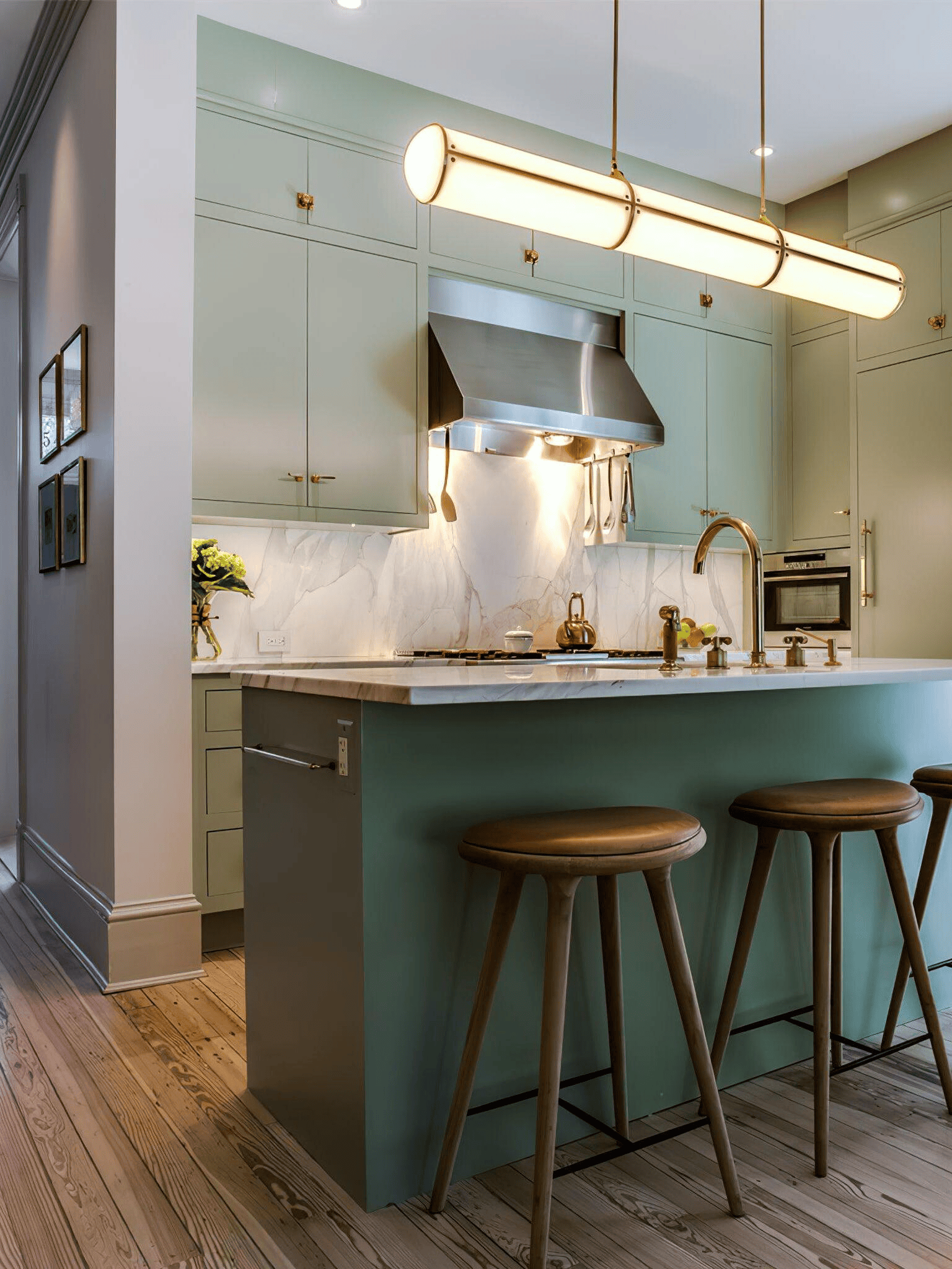 Modern kitchen island lighting with a sleek gold and white cylinder pendant over a green marble countertop.