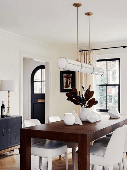 Warm home dining area with a modern white tube pendant light hanging above a dark wood table and white chairs.