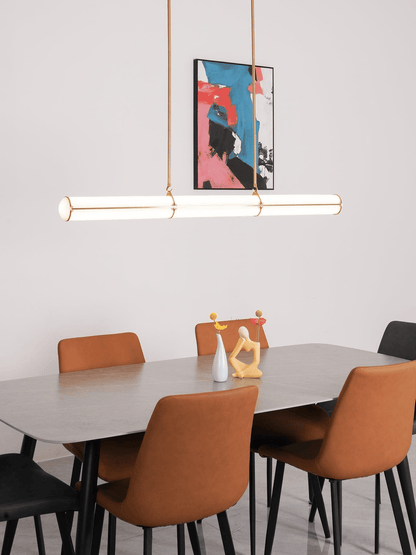 Minimalist dining room featuring a long horizontal glass tube pendant lamp over a grey table with orange chairs.