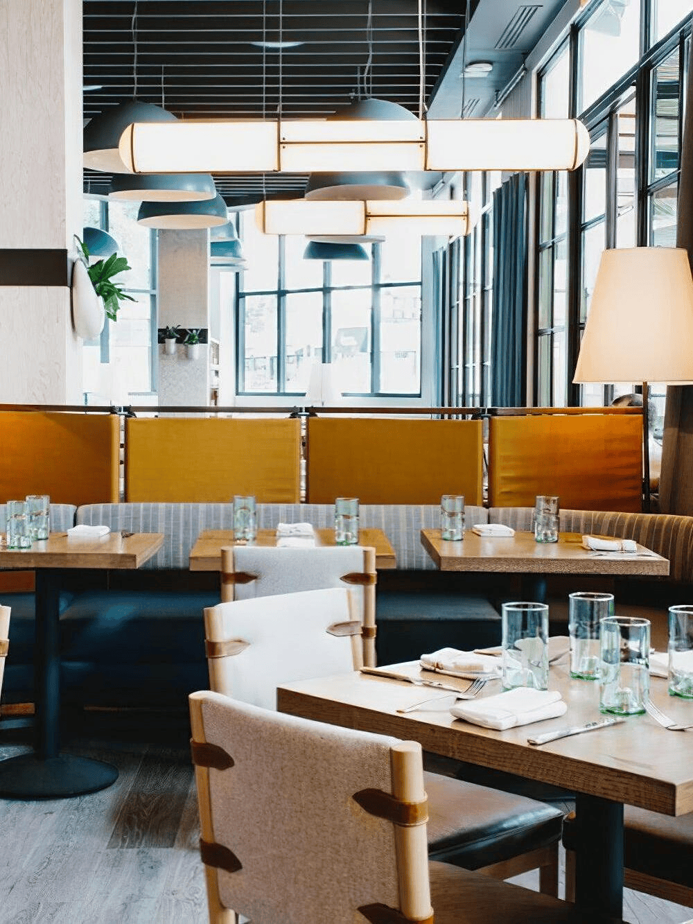 Contemporary restaurant interior lighting with linear capsule pendant lights over wooden booths and tables.