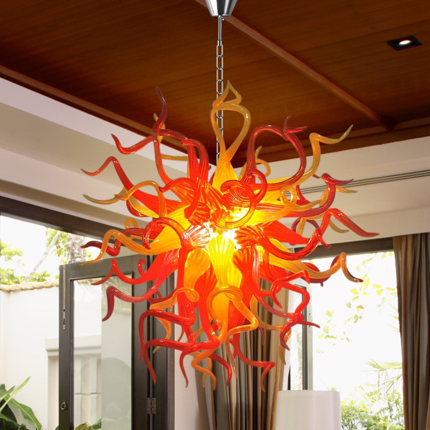 Large red and orange hand blown glass chandelier in a modern high-ceiling area.