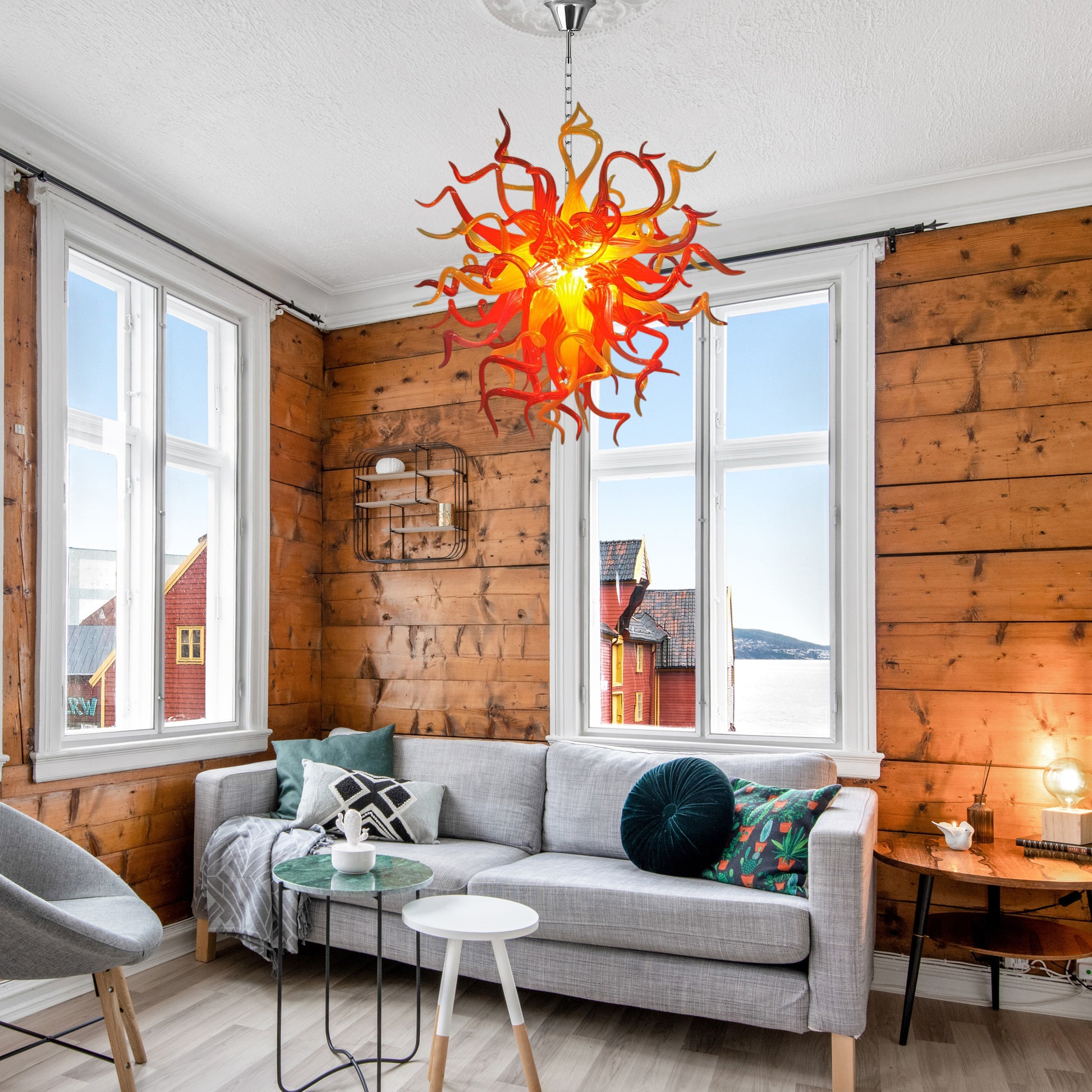 Red and orange abstract hand blown glass chandelier in a cozy wooden living room.
