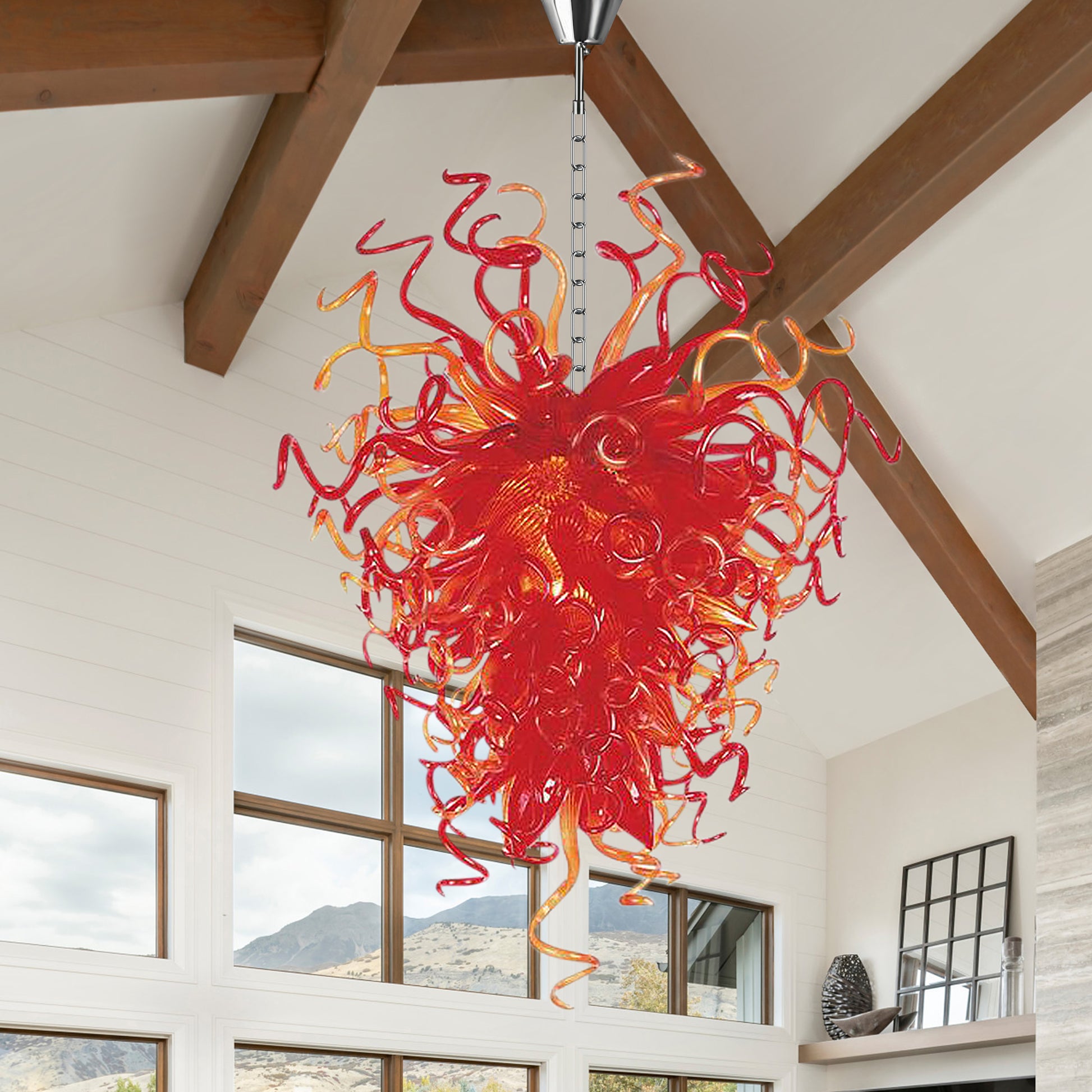 Long red and orange hand blown glass art chandelier in a modern high-ceiling room with large floor-to-ceiling windows.