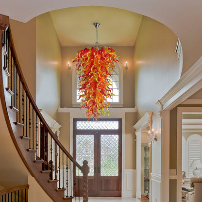 Custom size red and yellow hand blown glass chandelier centerpiece in a grand entryway/foyer with a curved staircase and high arched ceiling.