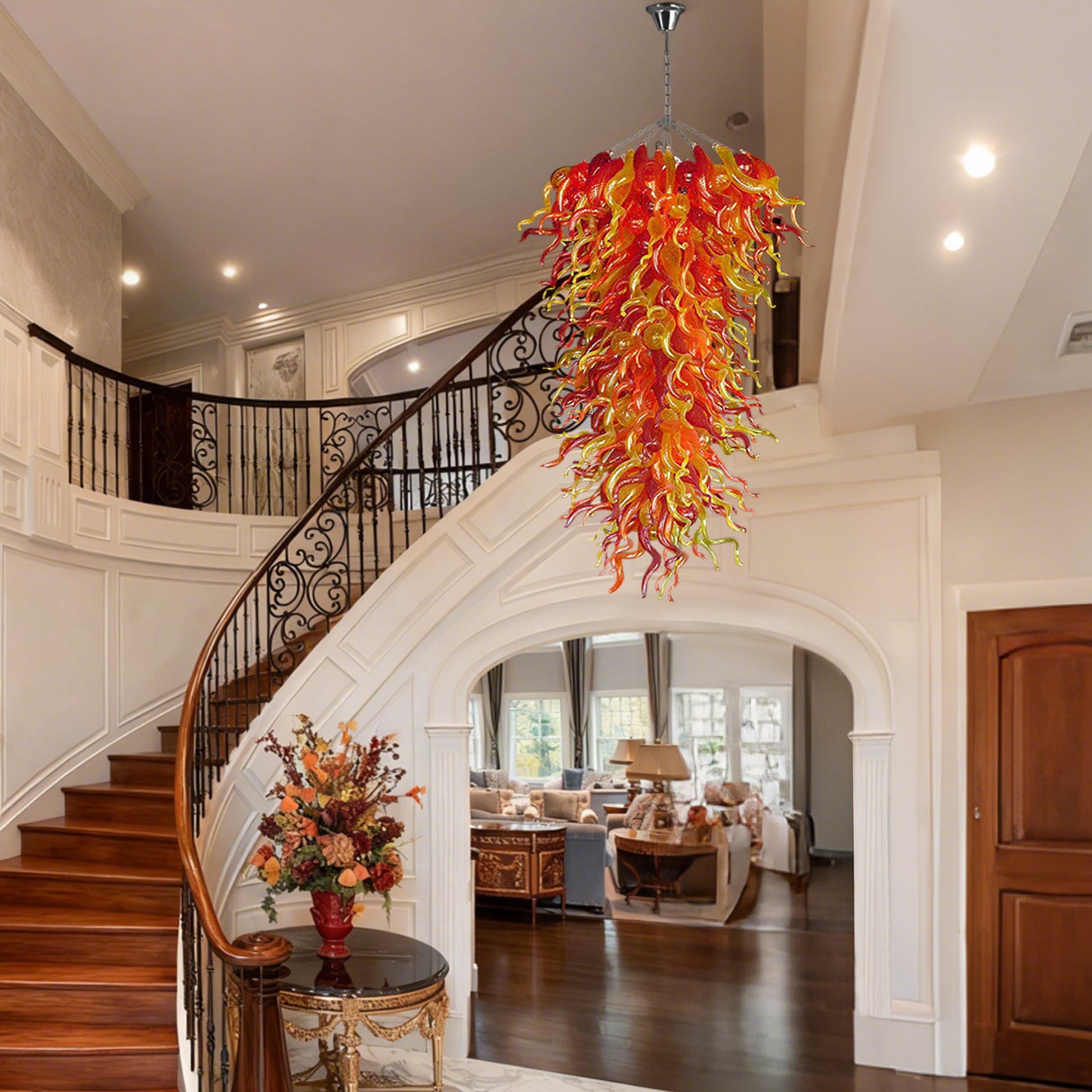 Spectacular hand blown glass chandelier illuminating a grand traditional foyer with a curved wooden staircase and high ceiling.