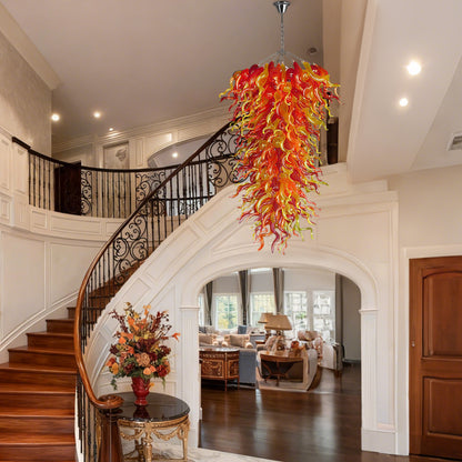 Spectacular hand blown glass chandelier illuminating a grand traditional foyer with a curved wooden staircase and high ceiling.