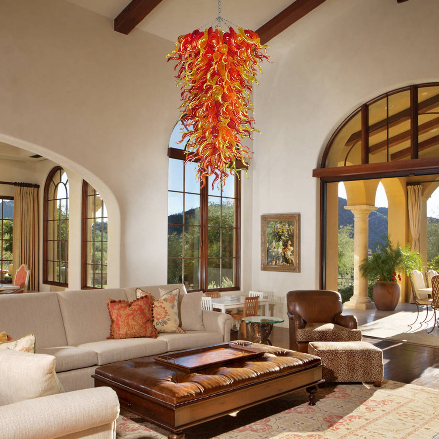 Large, vibrant red and yellow hand blown art glass chandelier as a focal point in a luxurious living room with a Mediterranean-style arched window.
