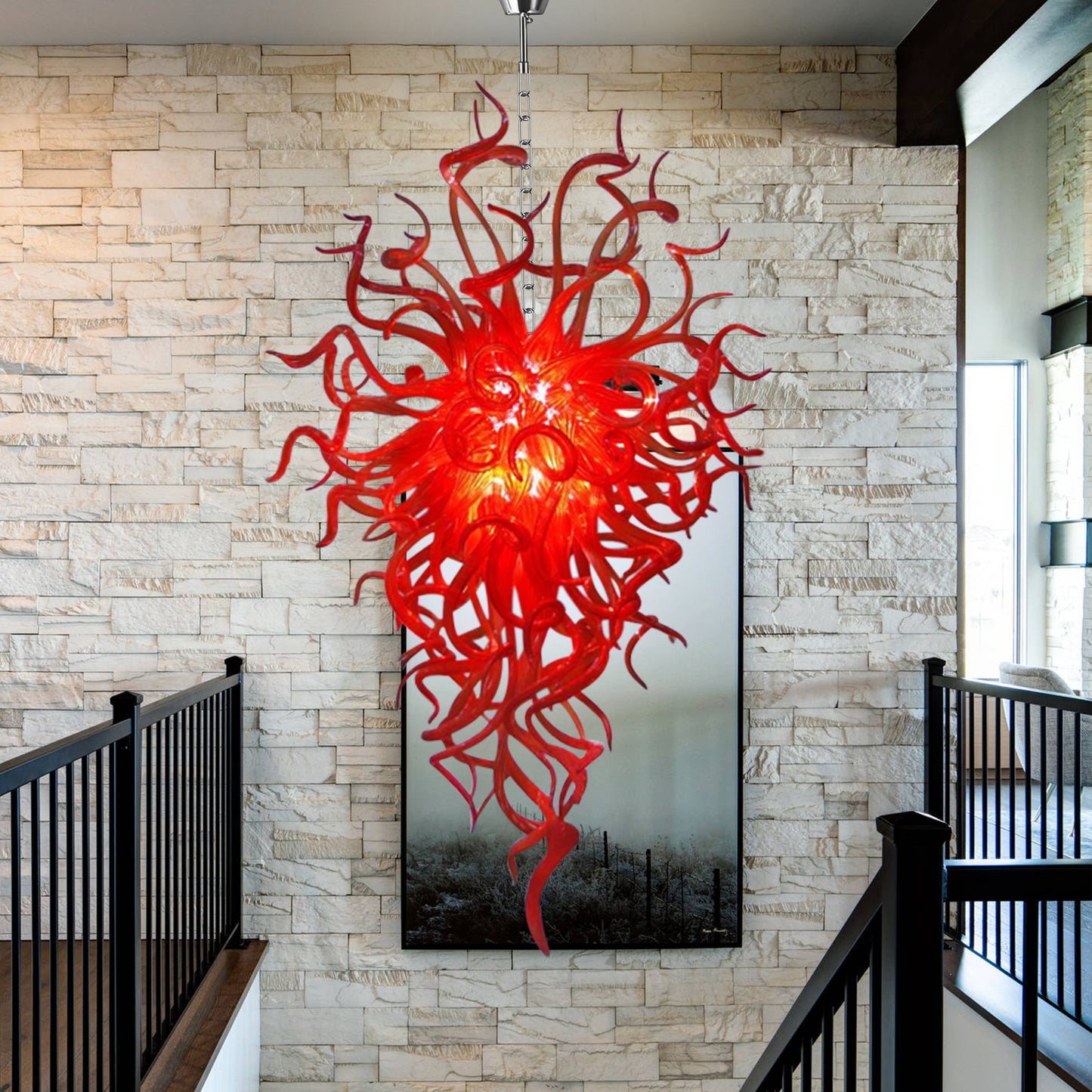 Extra-long red hand blown glass chandelier hanging near large contemporary windows.