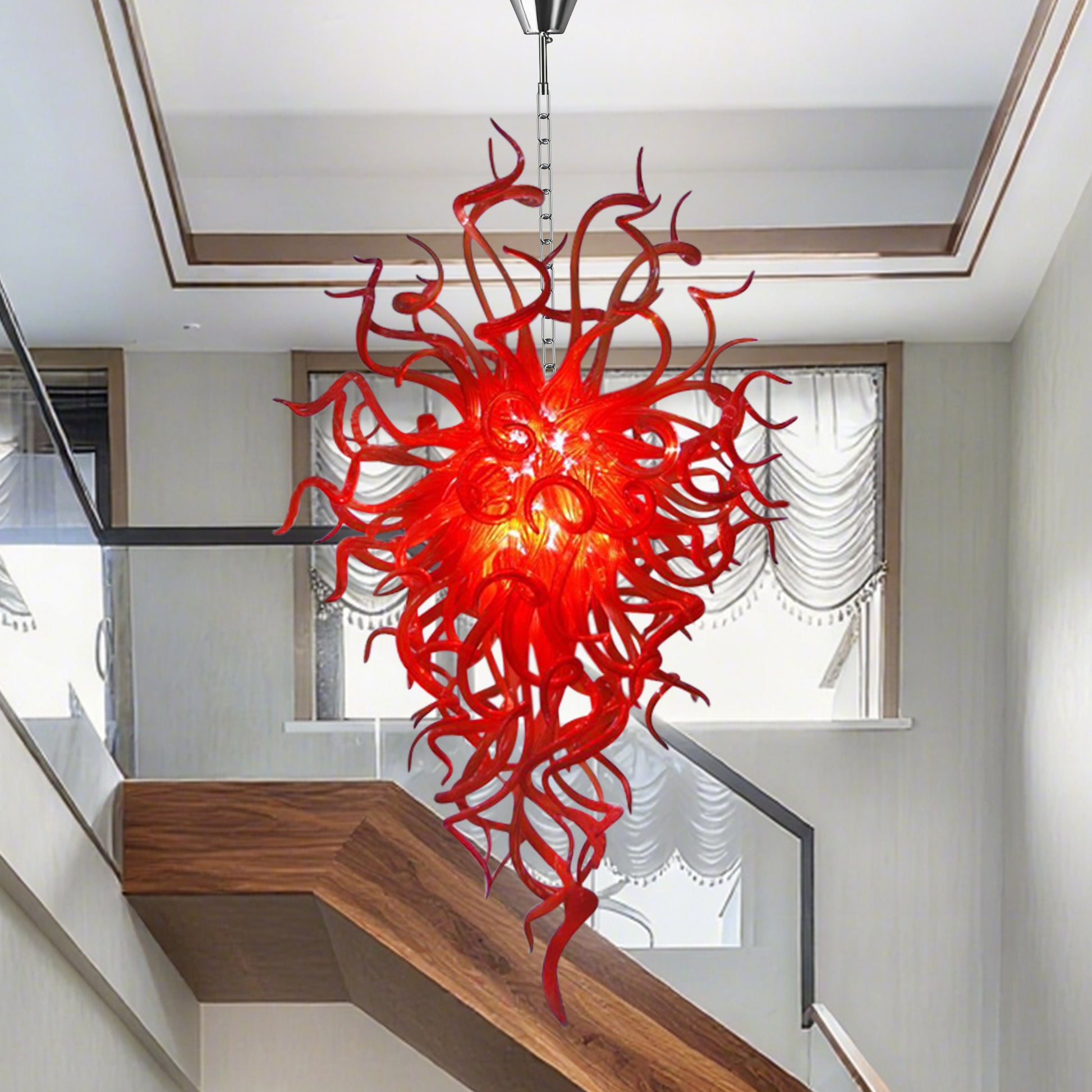 Red sculptural hand blown glass chandelier in an entryway over a modern wooden staircase.
