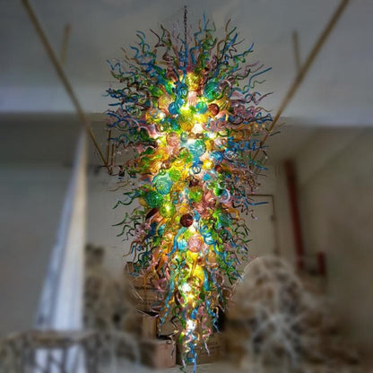 Close-up installation view of the giant vertical glass sculpture in a high-ceiling atrium, highlighting the density and scale of the hand-blown multicolor elements.