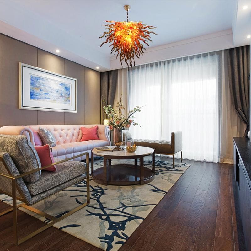 Luxury contemporary living room featuring a vibrant orange artistic glass chandelier hanging above a designer coffee table and plush seating.