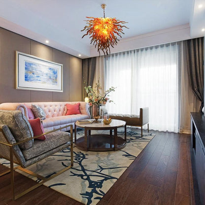 Luxury contemporary living room featuring a vibrant orange artistic glass chandelier hanging above a designer coffee table and plush seating.