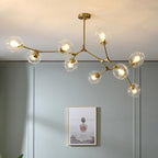 Modern gold branch chandelier with clear glass globes installed on a neutral grey wall in a minimalist room.