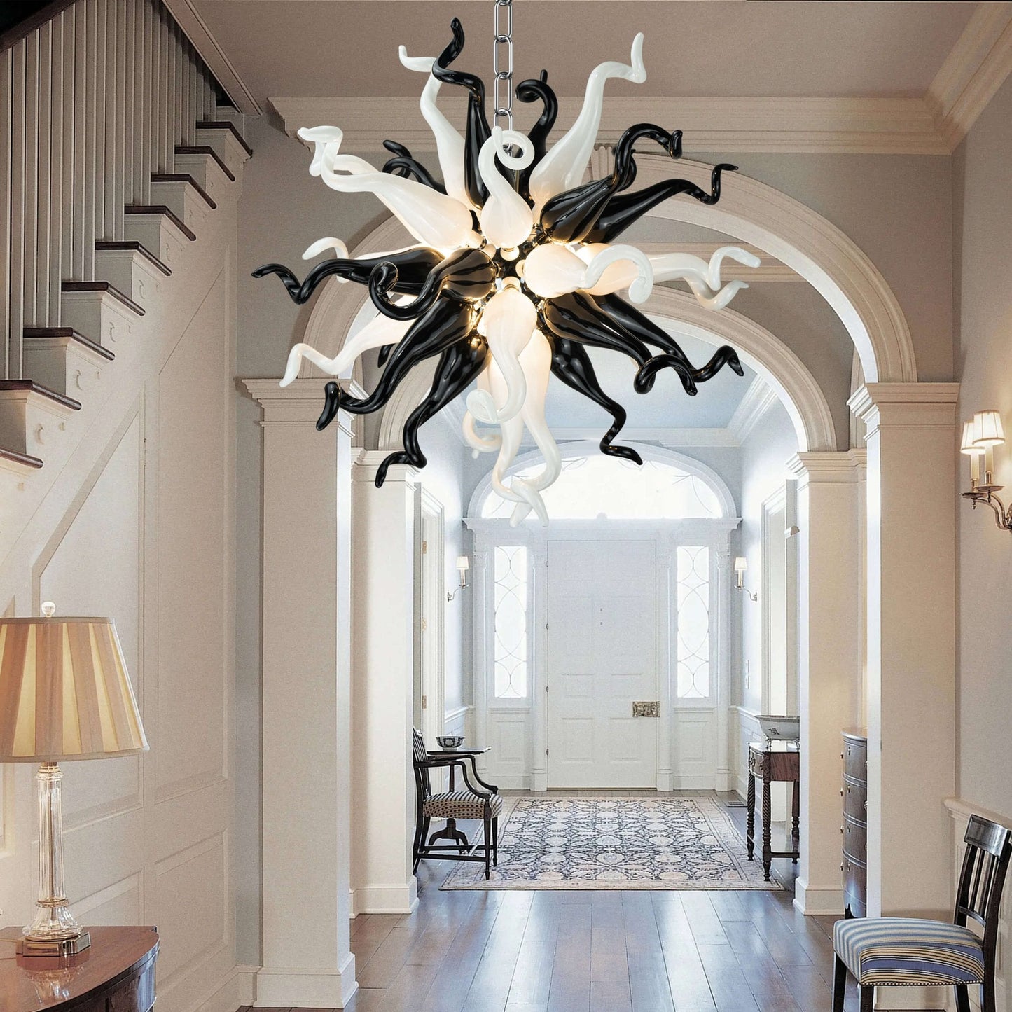 Modern black and white starburst glass chandelier hanging in a classic white luxury hallway with arched doorways.