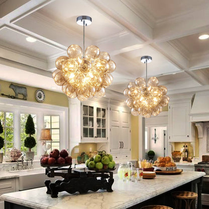Two Amber Bloom glass sphere chandeliers hanging above a large white marble kitchen island in an open-concept home.