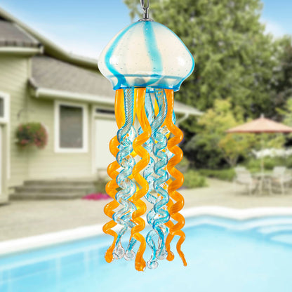 Blue and orange glass jellyfish wind chime hanging by a swimming pool in a bright sunny garden.