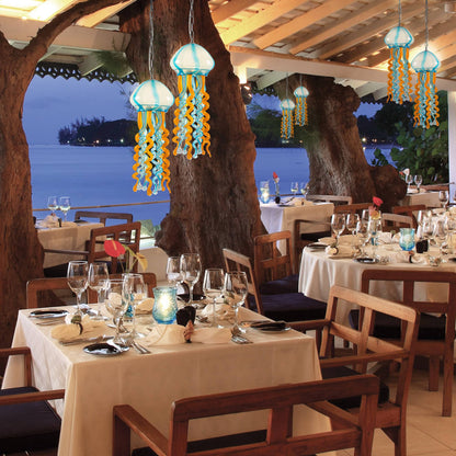 A cluster of jellyfish glass hanging lamps over a wooden dining table in a coastal resort restaurant.