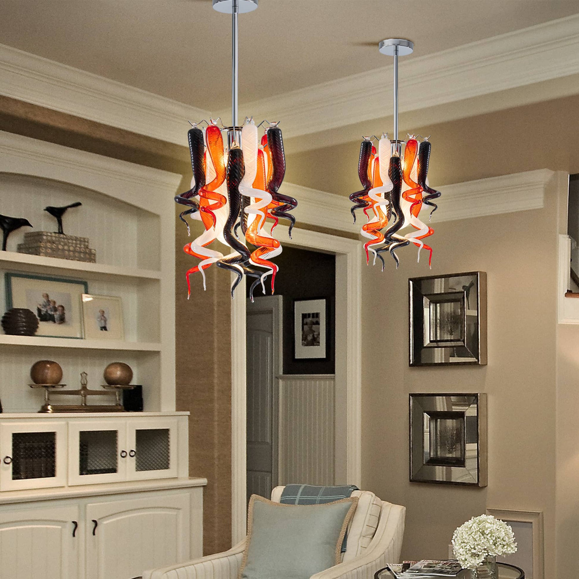 Dual miniature blown glass chandeliers installed over a stylish white kitchen cabinet area.