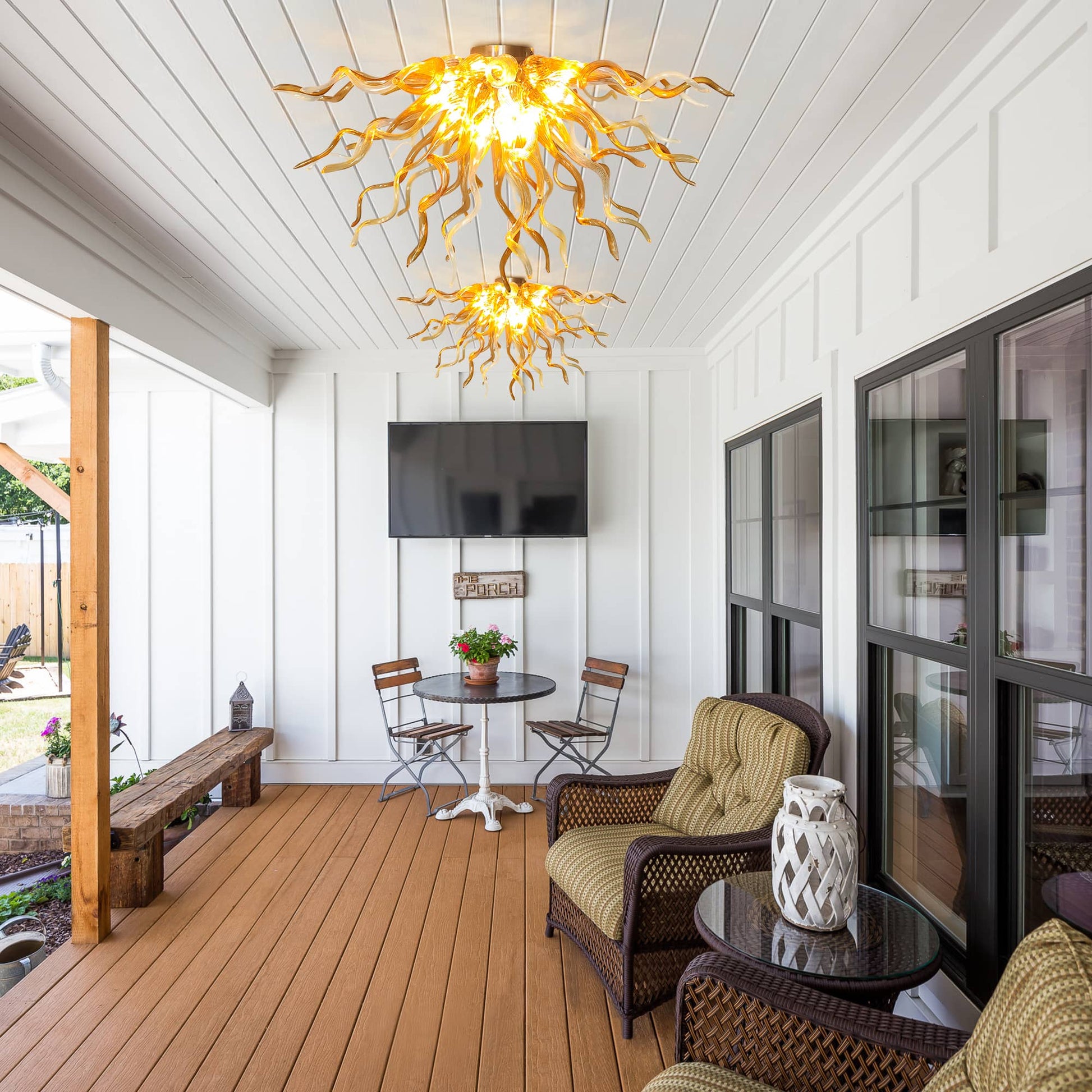 Long sunroom hallway and sitting area with the low-profile amber glass ceiling sculpture illuminating a cozy space with armchair seating and large windows.