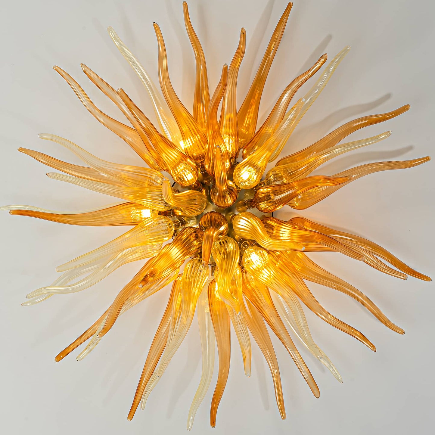 Direct view of a glowing orange glass starburst chandelier, mimicking a sunburst with warm golden light.