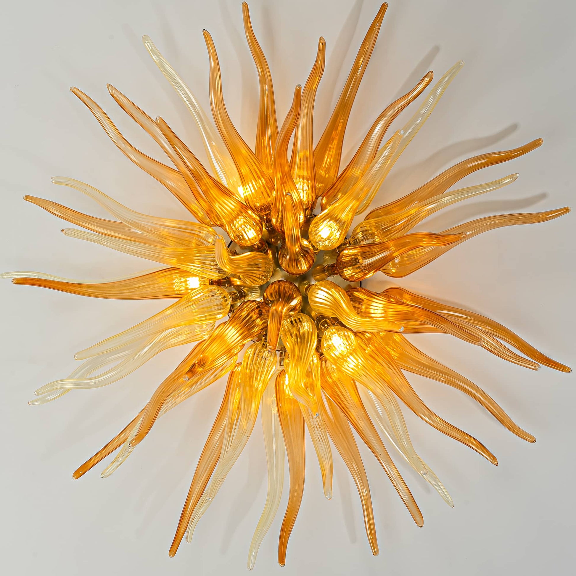 Direct view of a glowing orange glass starburst chandelier, mimicking a sunburst with warm golden light.