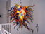 Detailed view of a vibrant Murano style blown glass chandelier with multicolored curly glass tendrils in a residential setting.