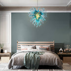 Artisan blue glass chandelier adding a serene oceanic touch above a contemporary upholstered bed.