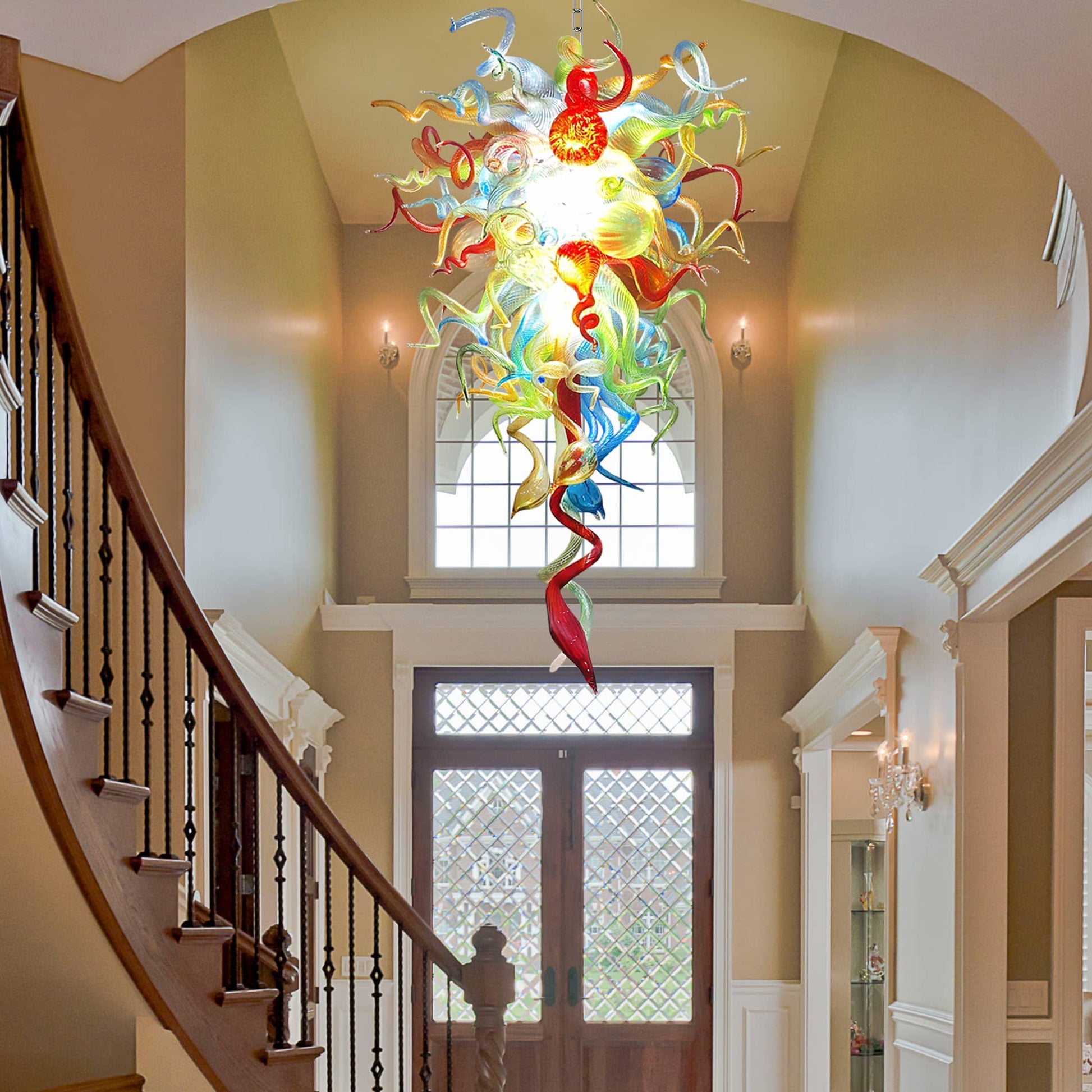 High-angle shot of a vibrant glass art chandelier hanging in a bright, open-concept foyer next to a dark wood staircase.