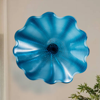 Large 12-inch Azure Blue hand-blown glass wall flower plate with ruffled edges and dark center on a white wall.
