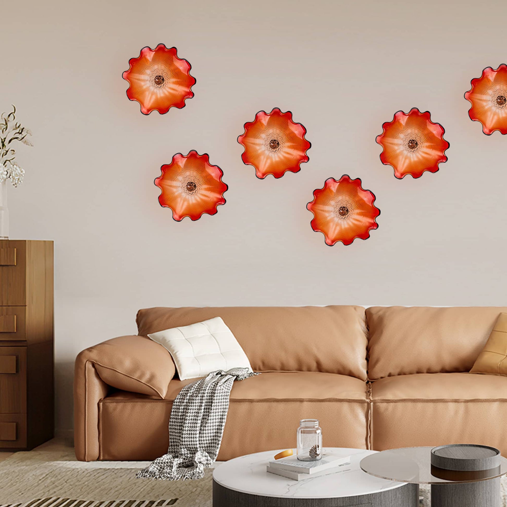 Five red art glass wall plates arranged in a cluster above a modern tan leather sofa.