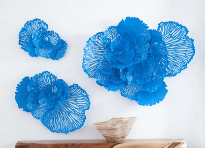 Three blue floral wall art pieces on a white wall with a wooden shelf below.