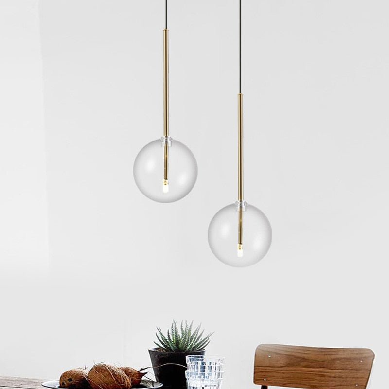 Minimalist Nordic pendant light with a clear hand-blown glass globe and a sleek brass rod suspension.