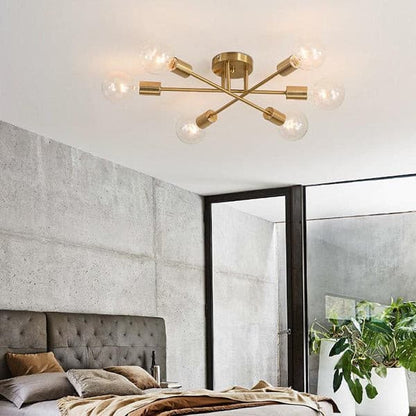 Sputnik linear brass ceiling chandelier illuminating a modern minimalist bedroom with a grey tufted headboard.