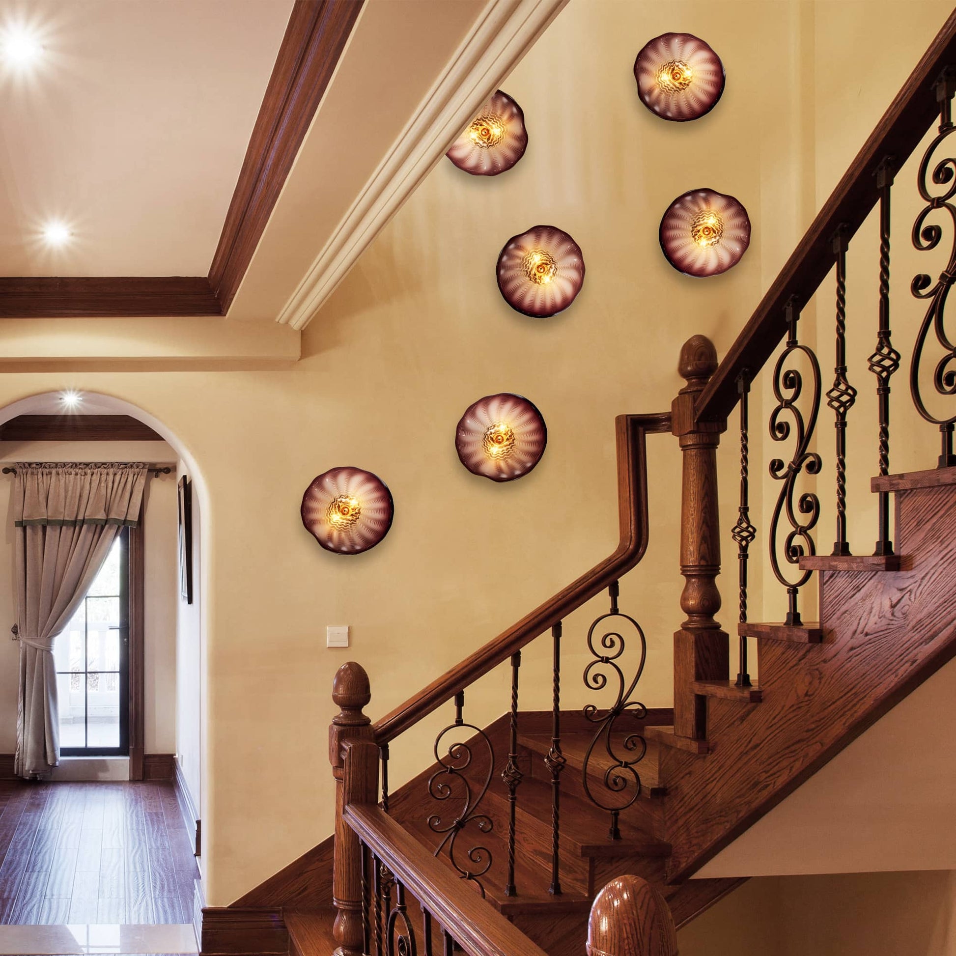A collection of amber and brown glass wall art plates illuminating a staircase wall in a high-end villa.