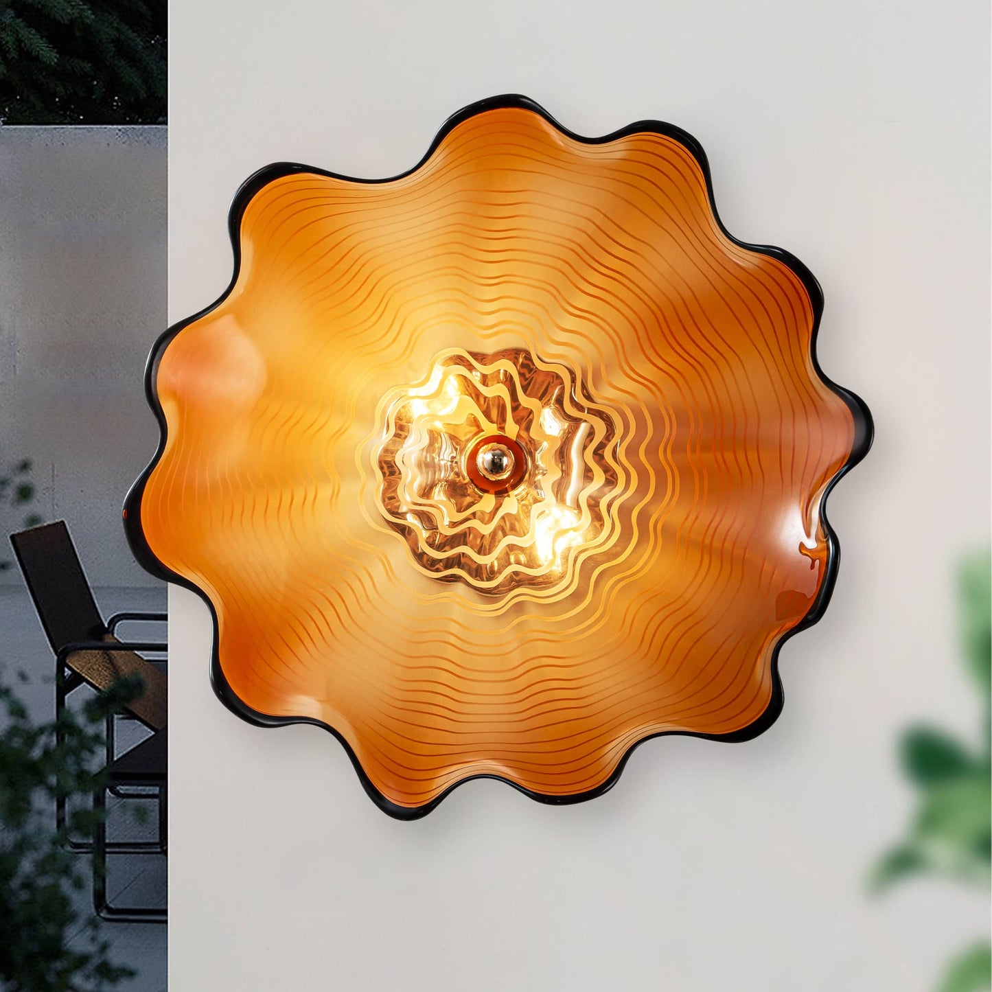 Frontal view of a single vivid orange glass wall plate with a black rim illuminated by warm LED light.