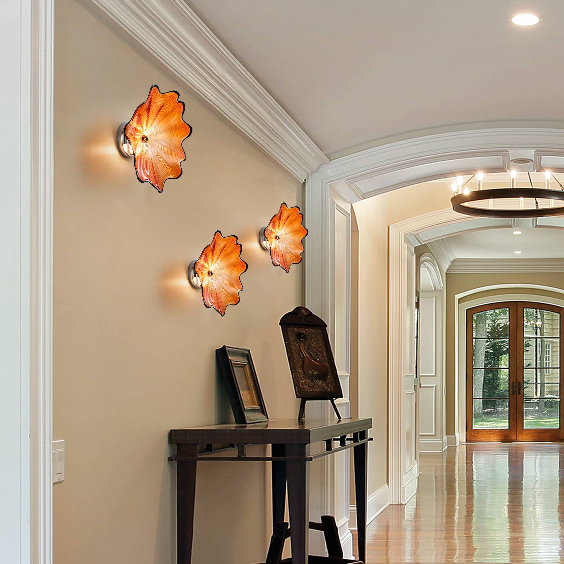 A trio of vivid orange Murano glass wall sconces arranged in a hallway above a black console table.