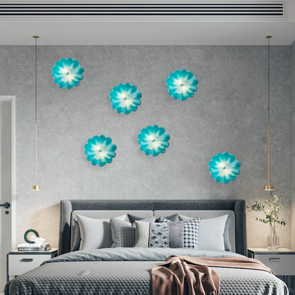 Bedroom accent wall with five backlit turquoise glass flowers arranged above a bed for a serene atmosphere.