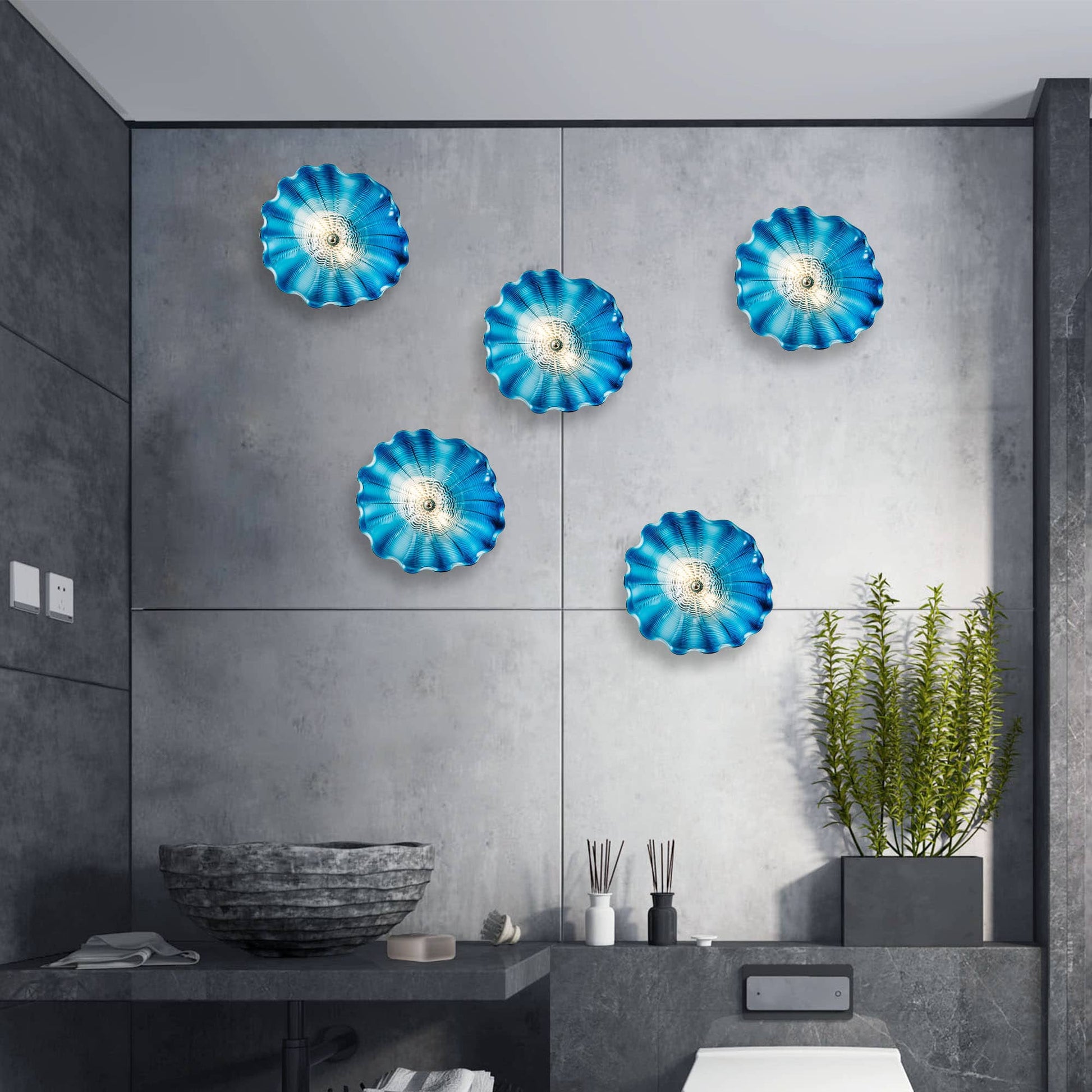 A cluster of six hand-blown blue glass flowers creating a wave-like pattern on a dark grey textured wall.