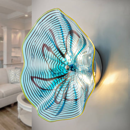 Side view of an illuminated aqua lotus glass wall lamp showing warm backlighting on a neutral wall.